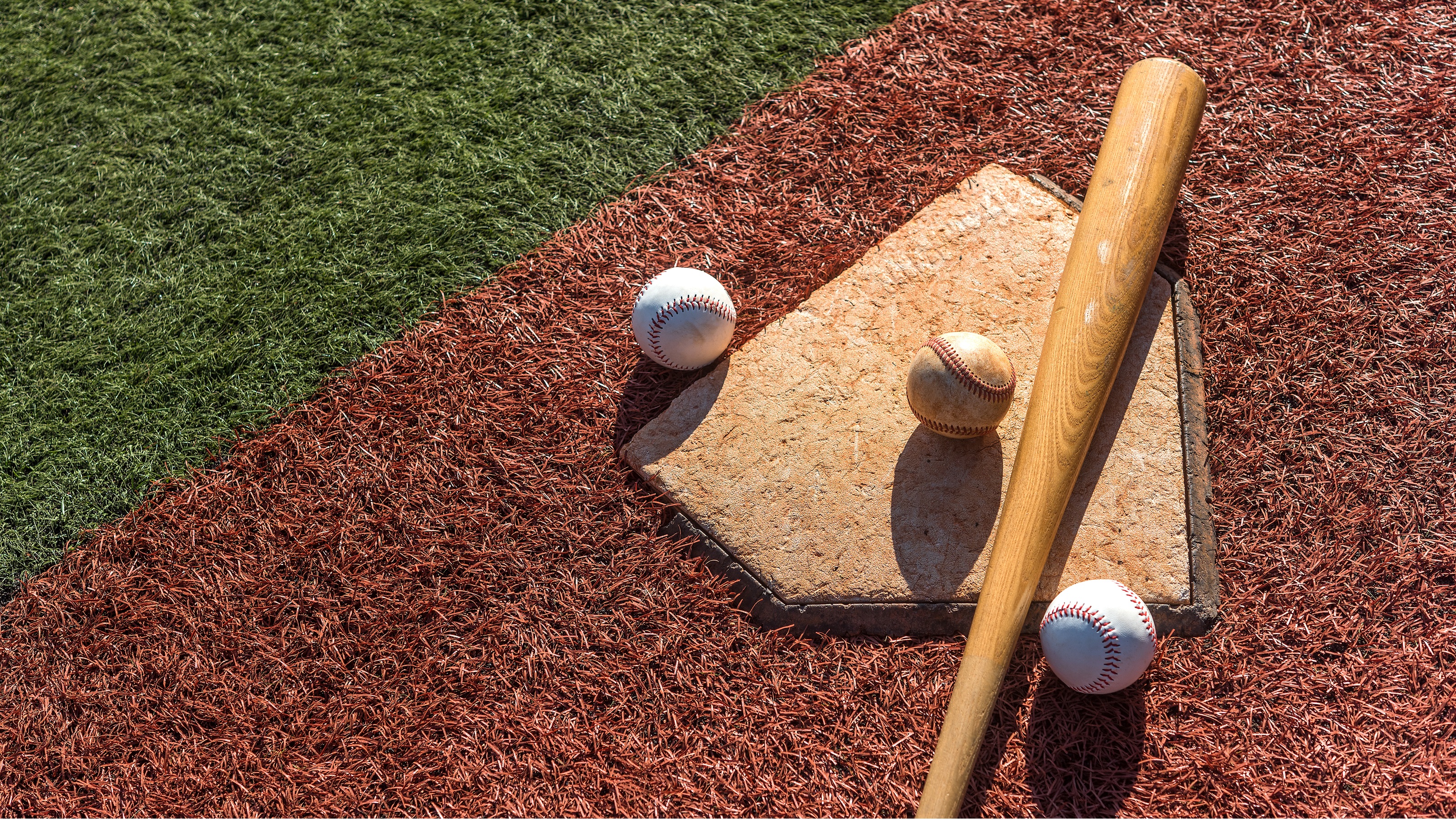 Tres pelotas de béisbol y un bate ubicados en el plato de home de un diamante de béisbol.
