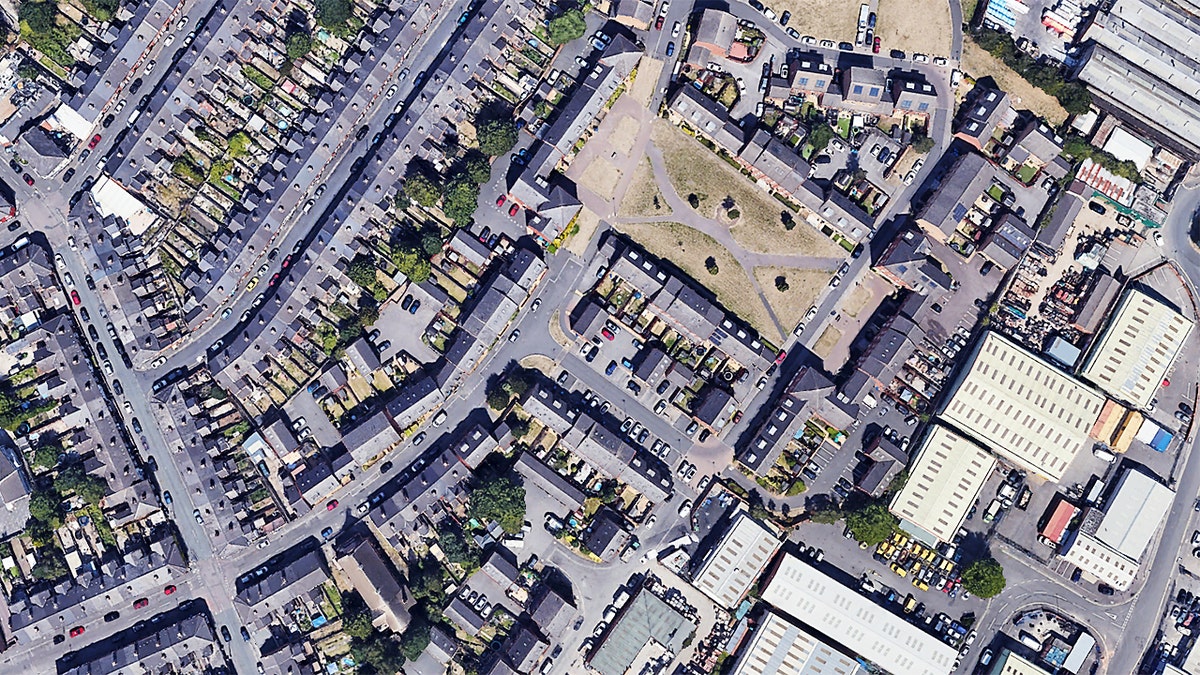 Vista aérea de calles residenciales y espacios verdes abiertos en Derby con automóviles estacionados a lo largo de varias calles.