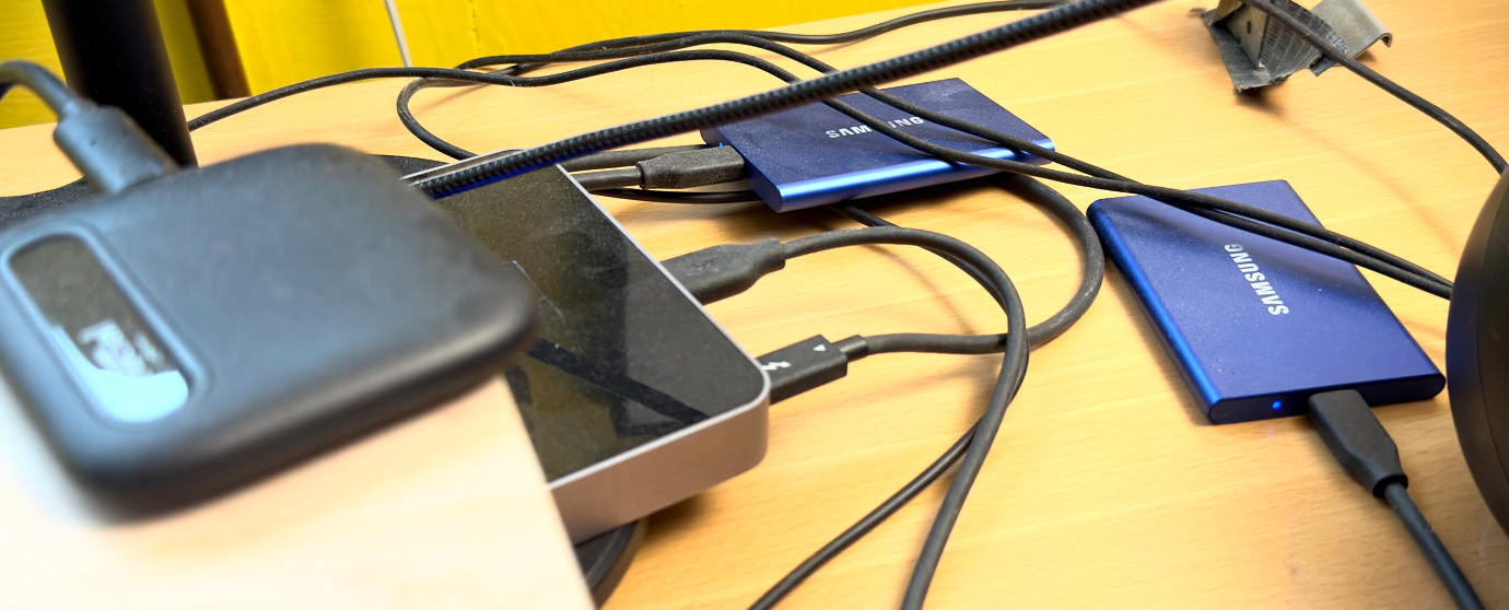 Una mesa de madera con un concentrador Thunderbolt y tres unidades SSD conectadas con cables desordenados