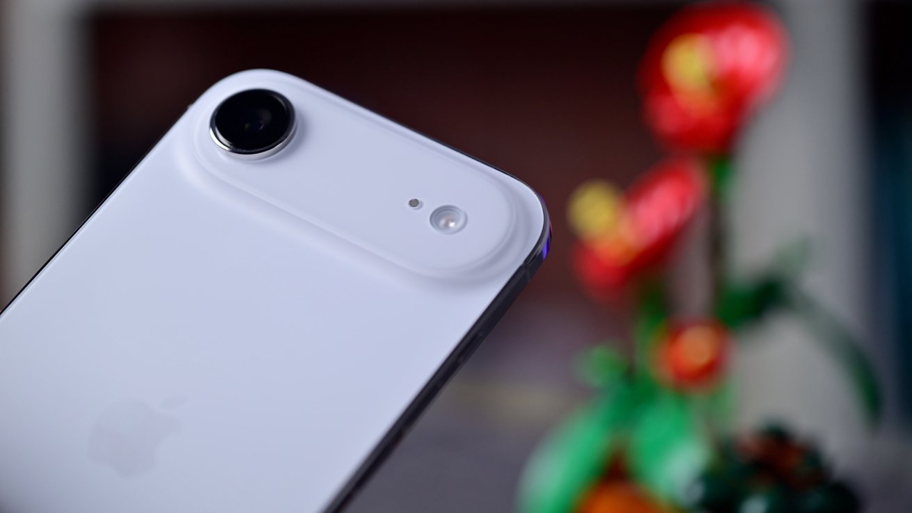 Primer plano de la cámara trasera y el módulo de flash de un iPhone Air blanco, con una planta colorida y borrosa en el fondo.