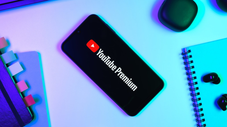 Un teléfono celular colocado sobre un escritorio entre dos portátiles diferentes; el teléfono móvil muestra el logotipo de YouTube Premium.